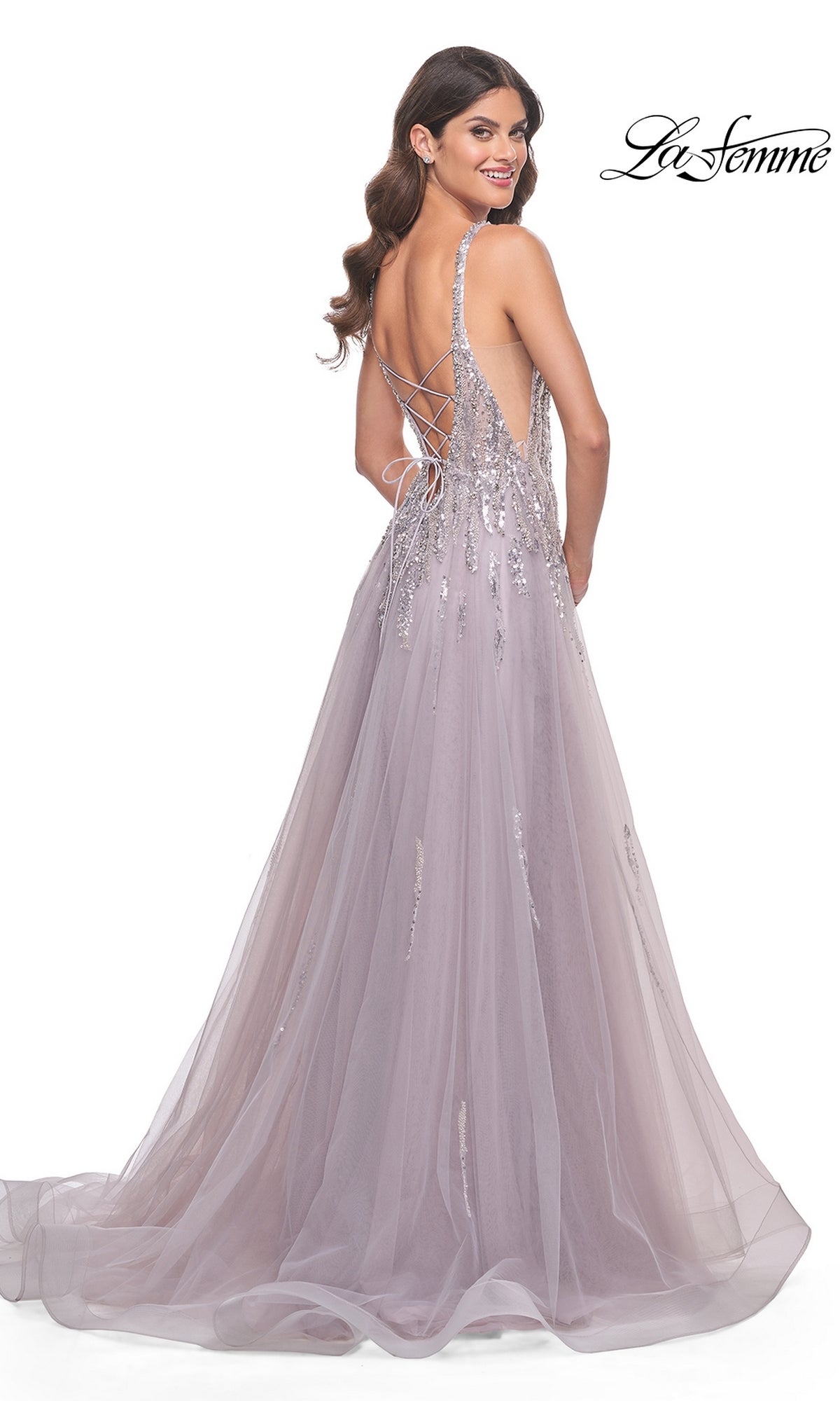 A woman stands smiling over her shoulder in the La Femme 31995, a sequined, floor-length mauve prom dress with an open lace-up back.
